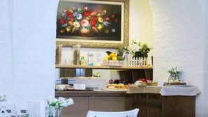 Una zona de menjador amb una paret de maó blanc, un quadre de flors sobre el taulell, i diversos aliments exposats.
