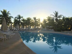 A poolside area with lounge chairs and umbrellas, surrounded by palm trees, reflecting the sunset. - Condo M Principe (Ixtapa)