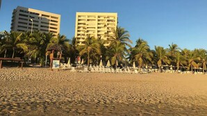 A beach with palm trees and a few buildings in the background. - Condo M Principe (Ixtapa)