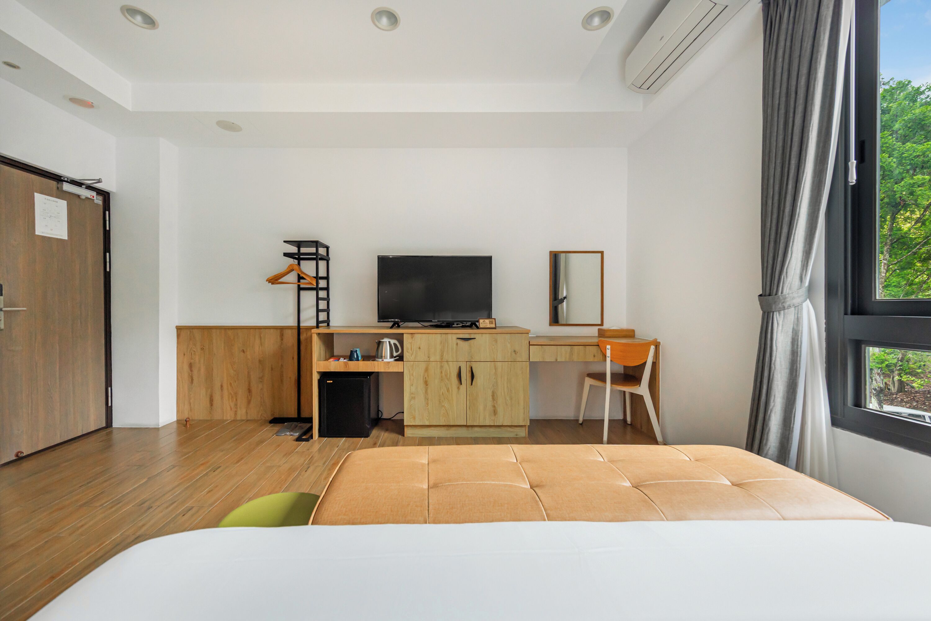 Une chambre d’hôtel moderne, équipée d’un lit, d’un bureau, d’une télévision et offrant une vue sur la verdure par la fenêtre.