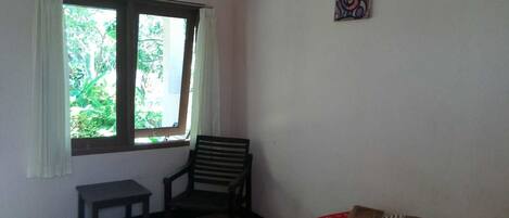A room with a bed, a chair, a small table, and a window with curtains.
