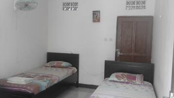 A small, simple room with two single beds, a wooden door, and a wall-mounted light fixture.