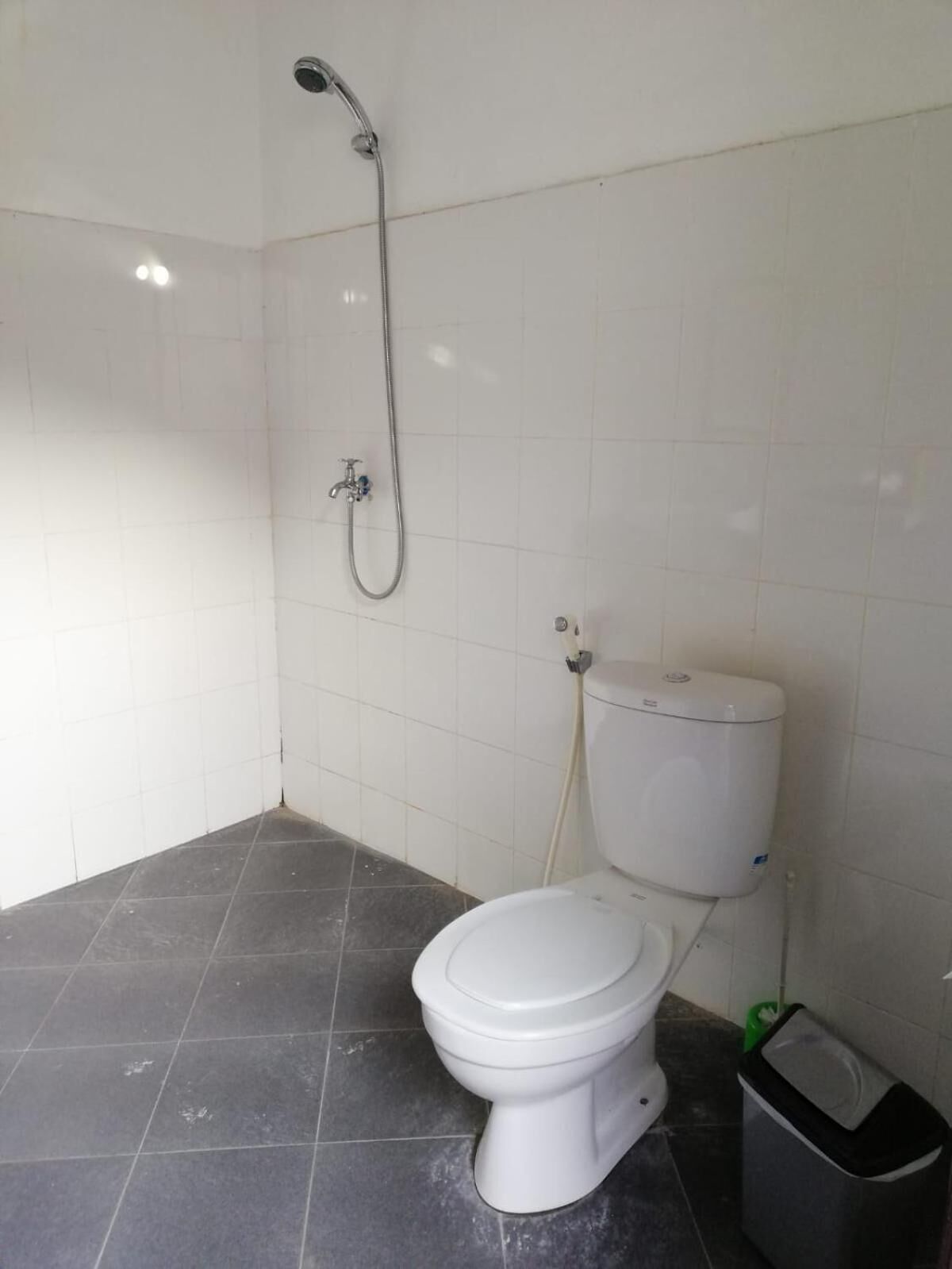 A small, clean bathroom with a toilet, a shower, and a trash bin.