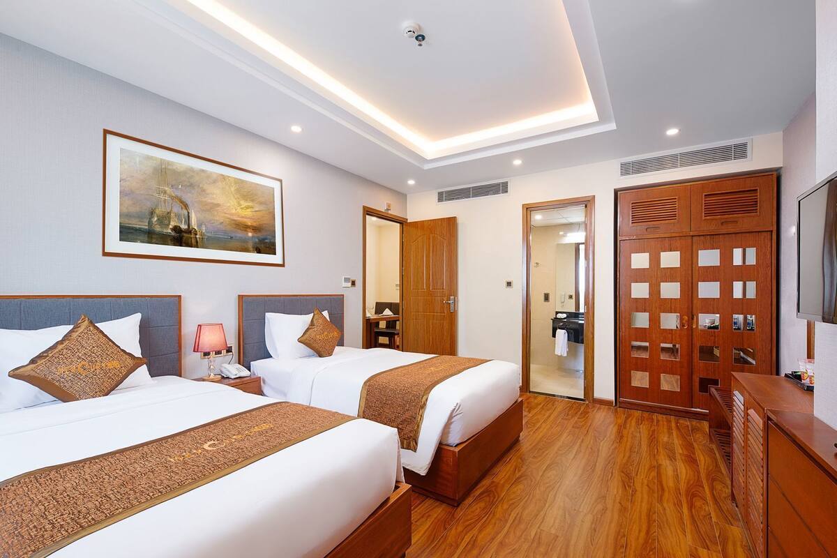 A hotel room with two beds, a painting on the wall, a wooden wardrobe, and a television.