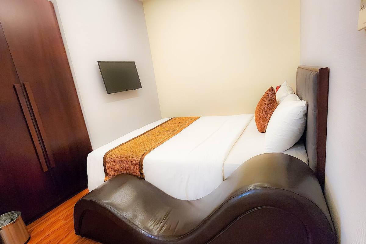 A modern hotel room with a bed, a flat-screen TV, a wooden floor, and a ceiling light.