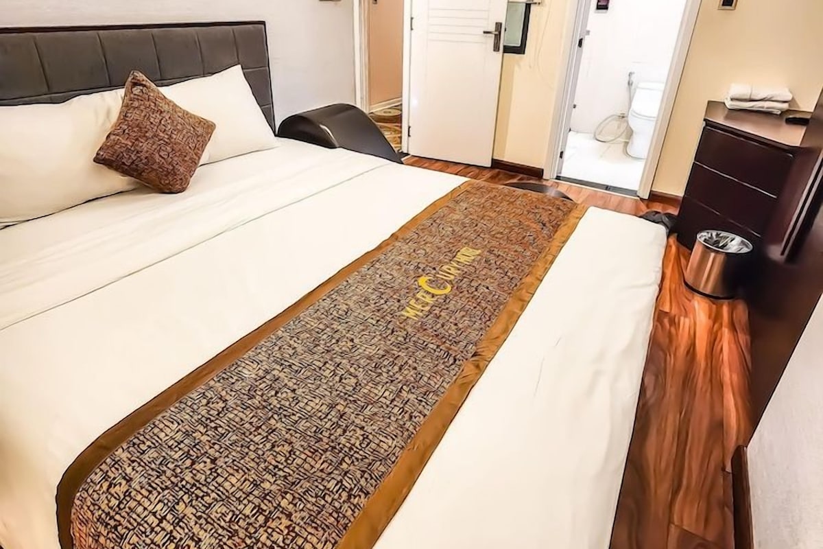 Quarto de hotel com uma cama, mesa de cabeceira, escrivaninha e banheiro visível por uma porta aberta.
