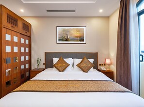 A hotel room with a large bed, a nightstand with a lamp, a framed picture on the wall, and a window with curtains. - Mercury Boutique Hotel (Da Nang)