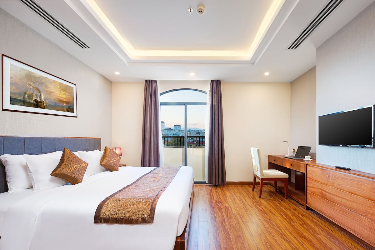 A hotel room with a bed, a desk, a chair, a TV, and a balcony with a city view.