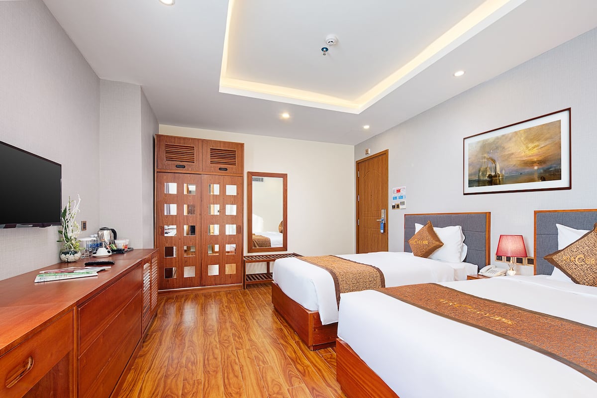 A hotel room with two beds, a wooden desk, a flat-screen TV, a large mirror, and a painting on the wall.
