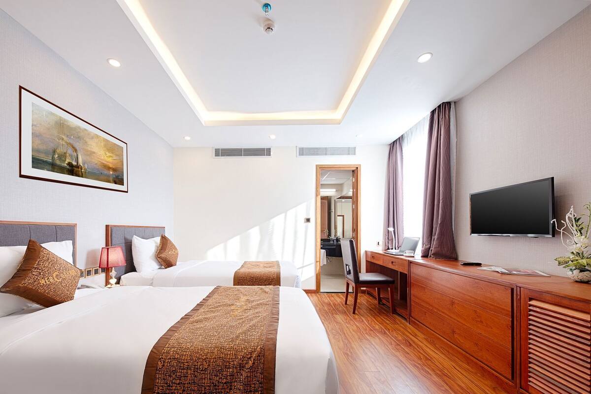 A hotel room with two beds, a desk, a television, and a painting on the wall.