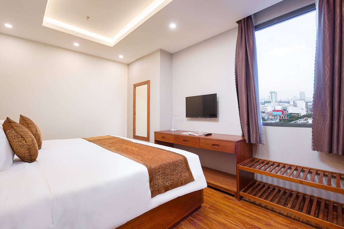 A hotel room with a bed, a desk, a TV, and a window with curtains.