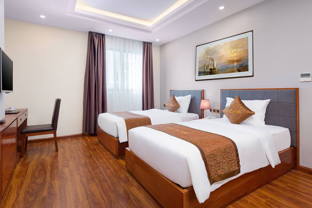 A hotel room with two beds, a desk, a chair, and a painting on the wall.