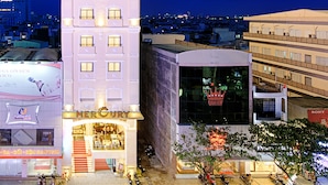 Um hotel alto com vários andares, entrada visível e estacionamento com diversos veículos.