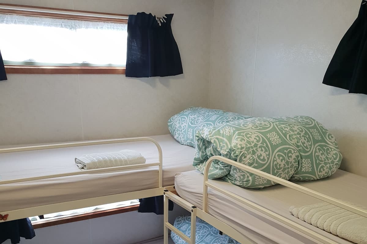 Een slaapkamer met stapelbed, raam, gestreepte kussens en een trap.