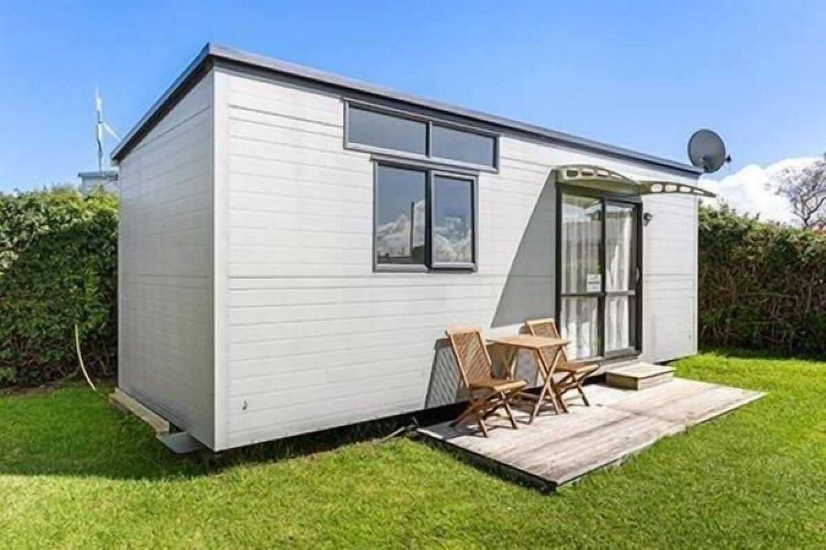 Een kleine, gelijkvloerse stacaravan met een terras, een schotelantenne en een raam.