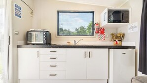 A compact kitchen with white cabinets, a built-in microwave, a toaster, and a refrigerator. - Port Waikato Holiday Park (Port Waikato)