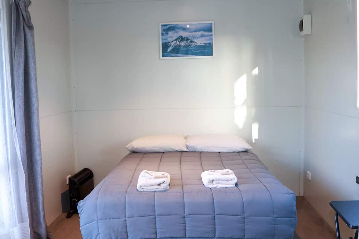 Een bed met een blauwe quilt, twee kussens en twee opgevouwen handdoeken.