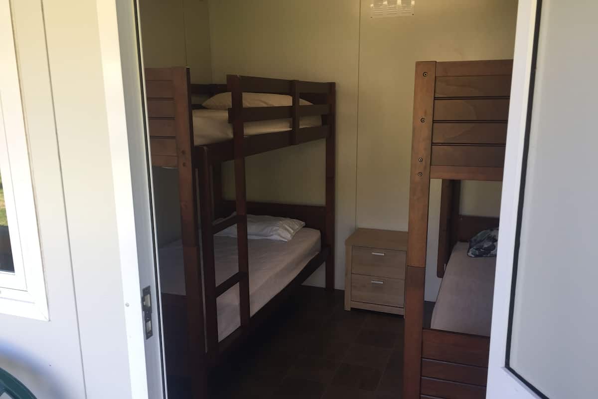 Een kleine kamer met stapelbedden, een klein houten kastje en een deur naar een andere ruimte.