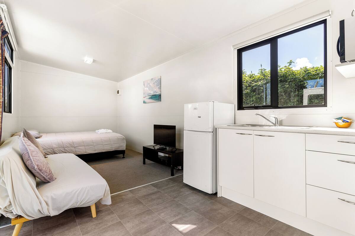 Een compacte, moderne kamer met een bed, een kleine kitchenette en een raam met uitzicht op groen.