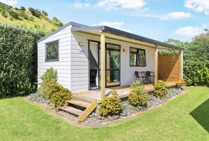A modern single-story house with a covered porch, a small deck, and a landscaped garden with shrubs and a wooden bench. - Port Waikato Holiday Park (Port Waikato)