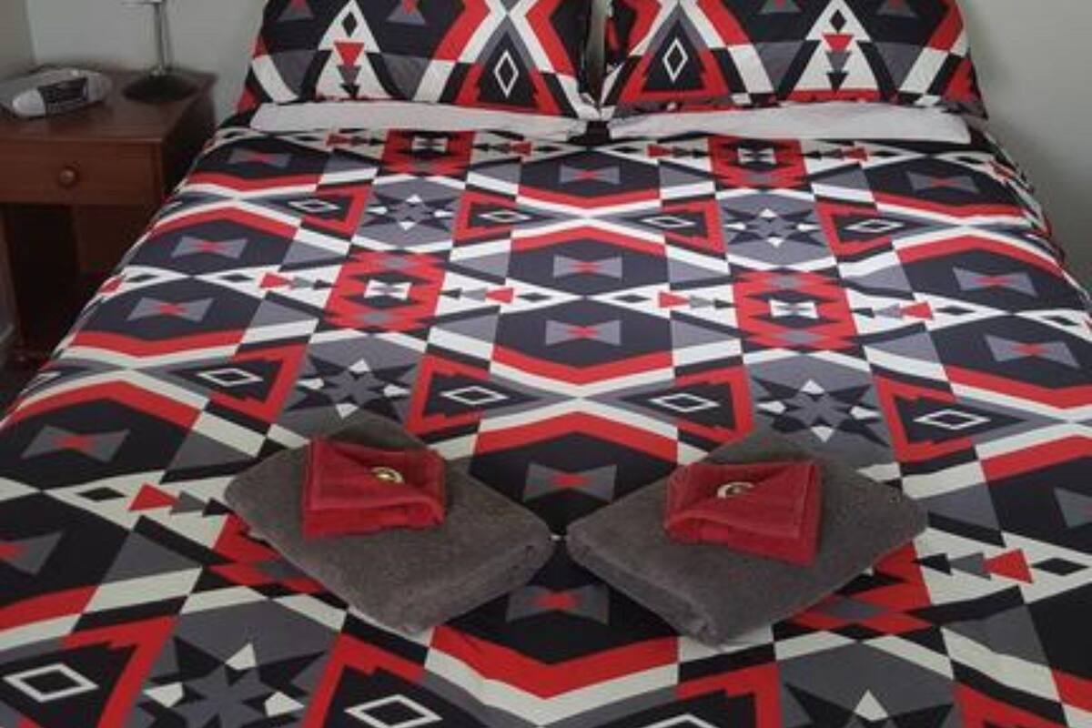 Een bed met een bedspreide met patroon, twee kussens en een nachtkastje met een lamp.