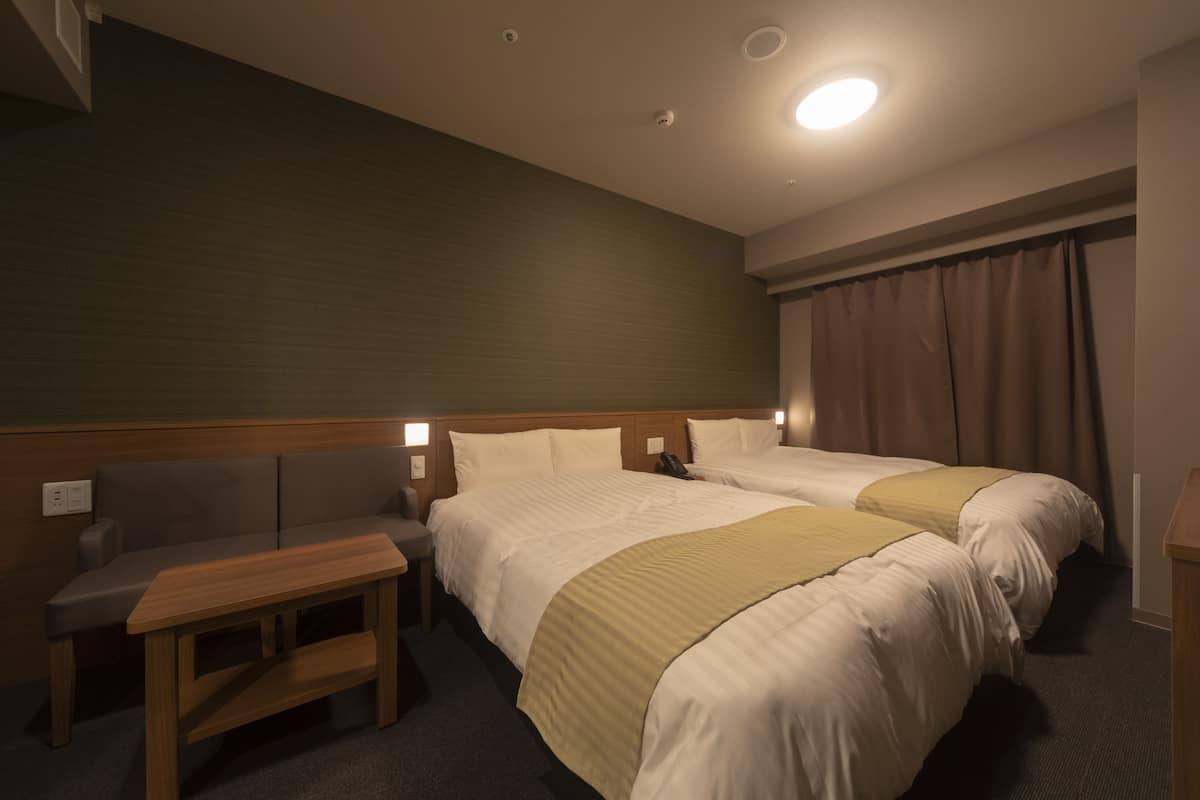 Ein Hotelzimmer mit zwei Betten, einem Holztisch, einer Couch und einem Schreibtisch.