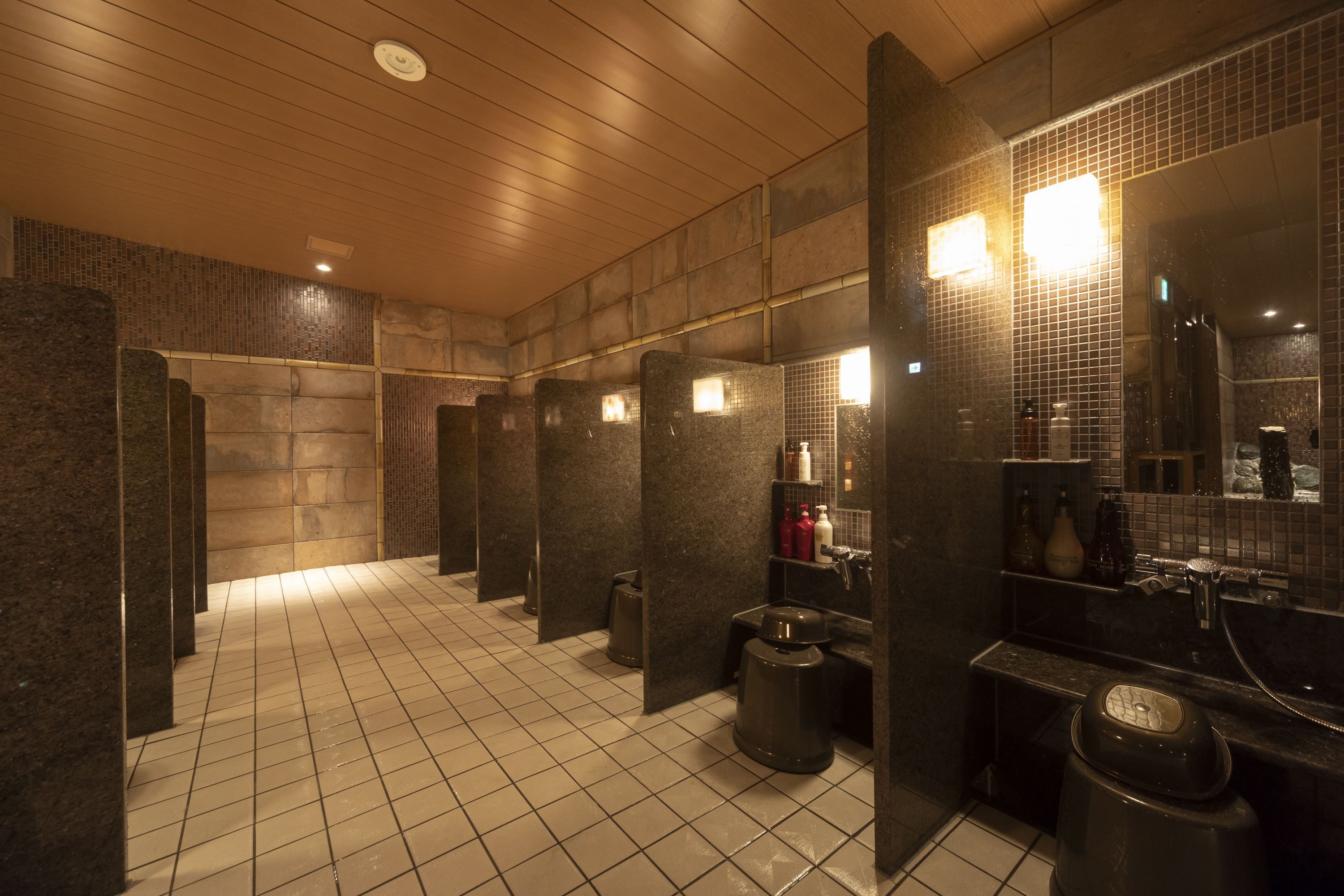 A public restroom with tiled floors, granite partitions, and a sink area with mirrors and toiletries.