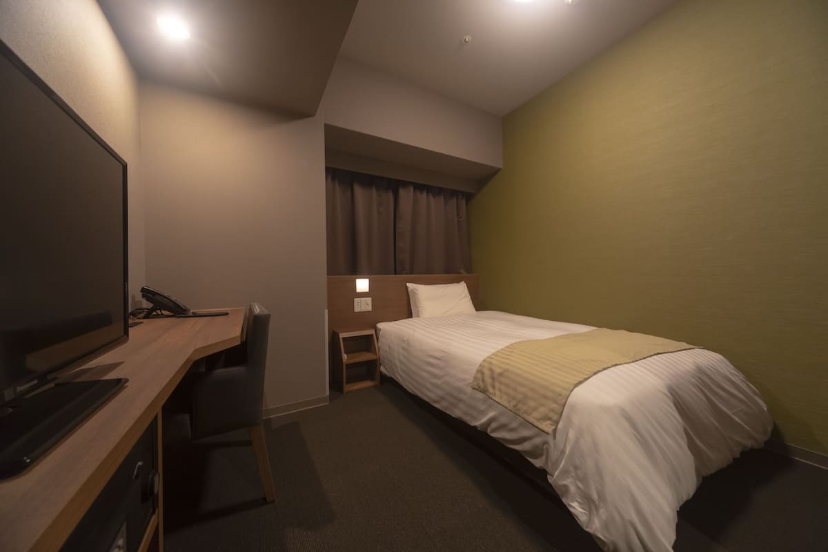 Ein Hotelzimmer mit einem Bett, einem Schreibtisch mit Computer, einem Fernseher und einem kleinen Regal.