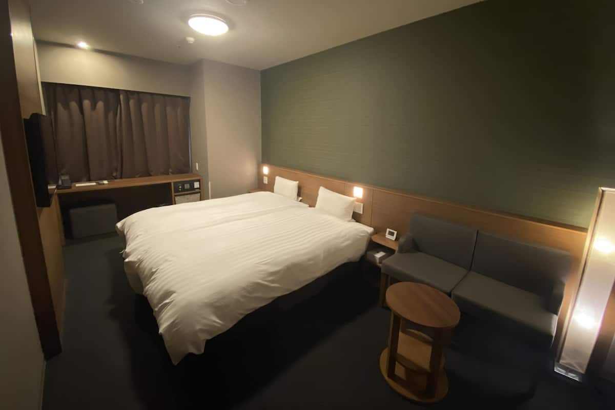 Ein Hotelzimmer mit einem großen Bett, einer kleinen Couch, einem runden Holztisch und einem Fernseher auf einem Schrank.