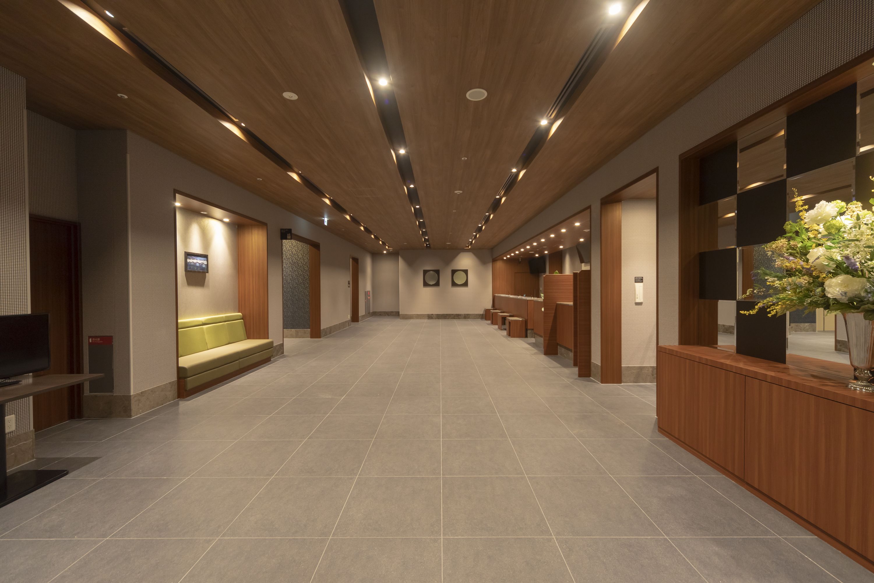 A spacious hallway with a wooden ceiling, tiled floor, and a reception area with a counter and seating.