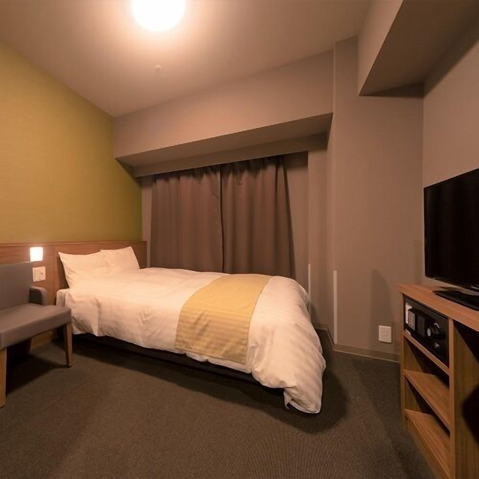 A hotel room with a bed, a bench, a television, and a window with curtains.