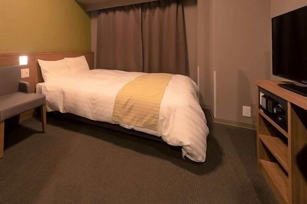 Ein Hotelzimmer mit einem Bett, einer Sitzbank, einem Fernseher und einem Fenster mit Vorhängen.