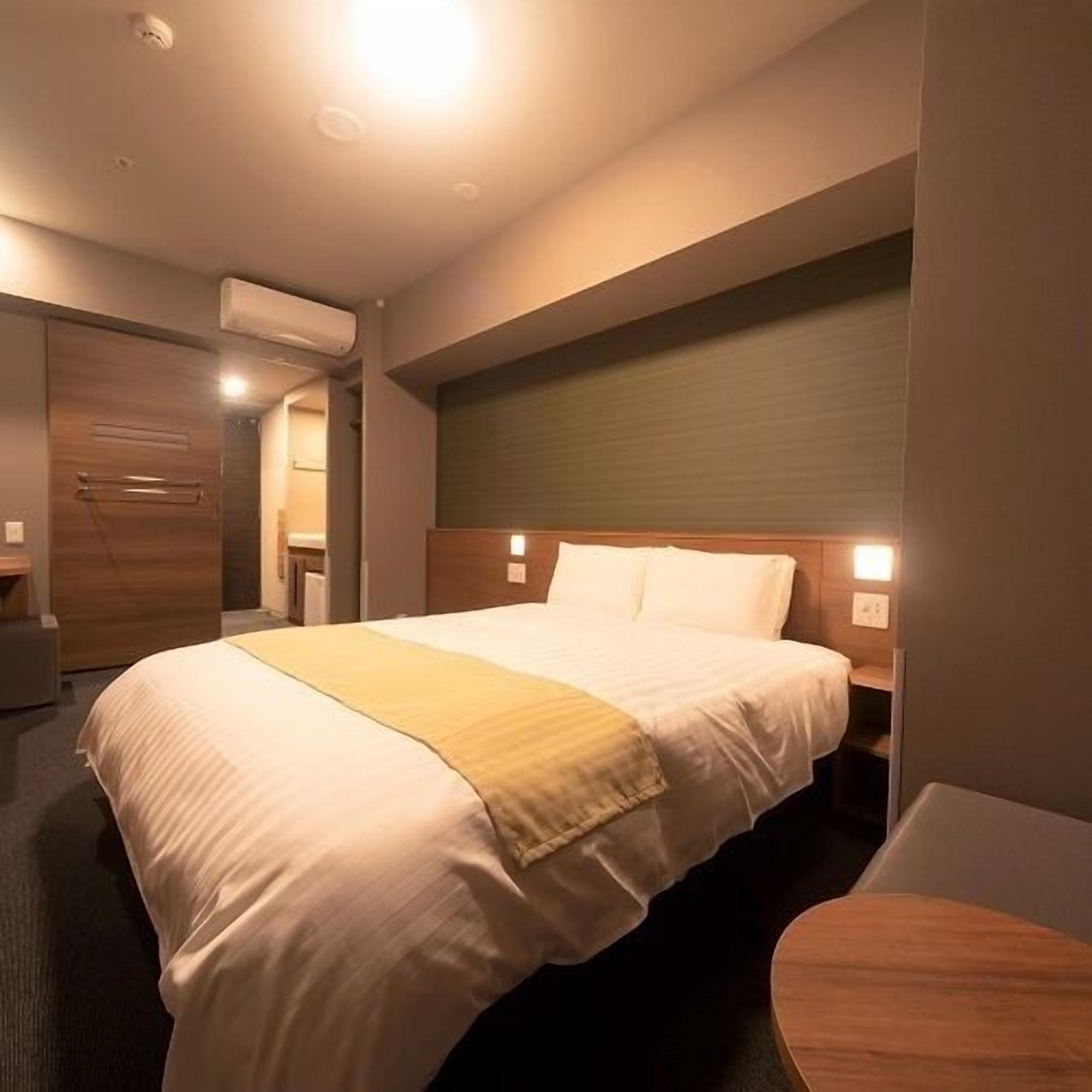 A hotel room with a large bed, bedside tables, a wooden headboard, and an air conditioning unit.