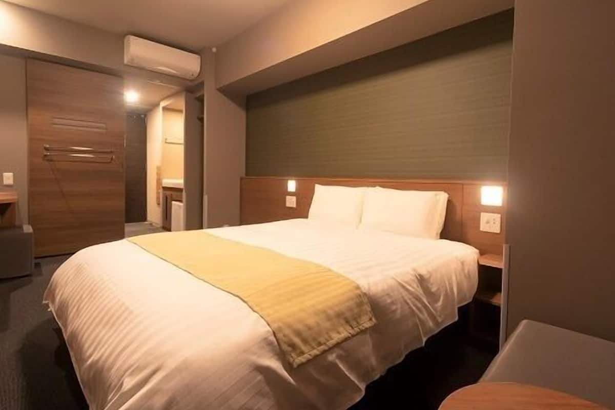 Ein Hotelzimmer mit einem großen Bett, Nachttischen, einem Holz-Kopfteil und einer Klimaanlage.