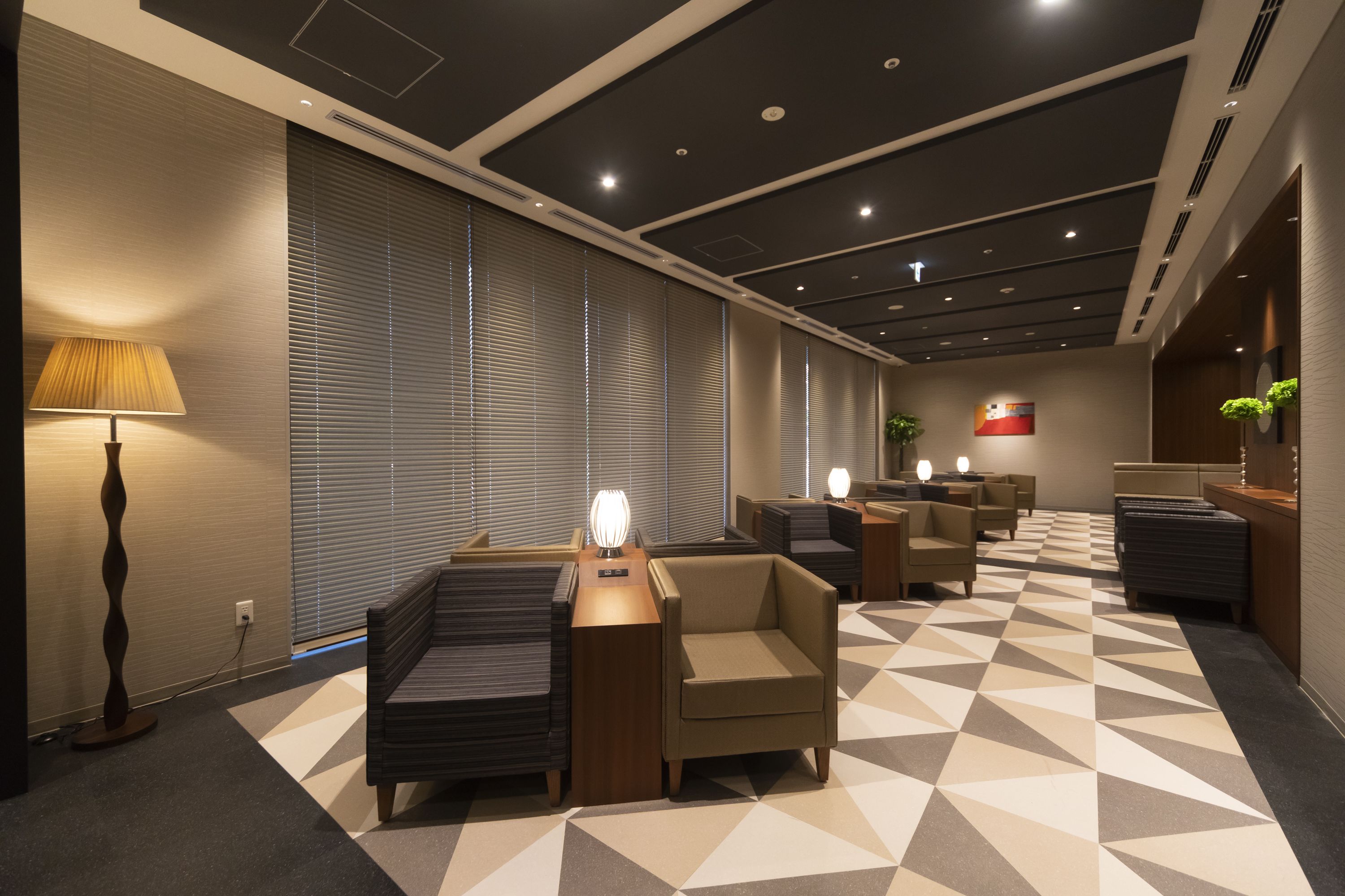 A modern hotel lobby with a geometric patterned floor, seating areas, and a reception desk.