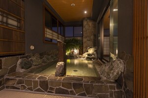 A stone hot spring bath area with a wooden ceiling and large windows.