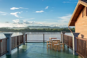 A wooden deck with a railing overlooking a body of water and distant mountains.