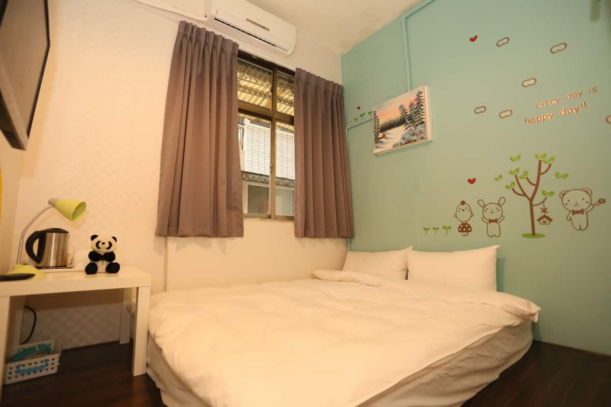 A bedroom with a bed, a desk with a lamp, a panda toy, and a window with curtains.