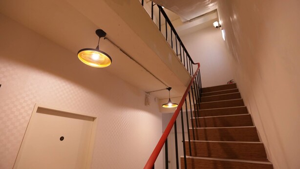 Una escalera de madera con barandilla roja que lleva a una puerta con pomo redondo.