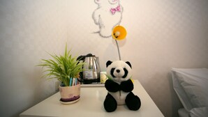 Un peluche de panda sobre una mesa blanca, con una planta en maceta y una tetera al fondo.
