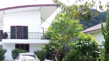 A two-story house with a balcony, surrounded by lush greenery and trees.