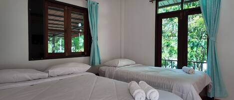 A room with two beds, a window with curtains, and a view of greenery outside.