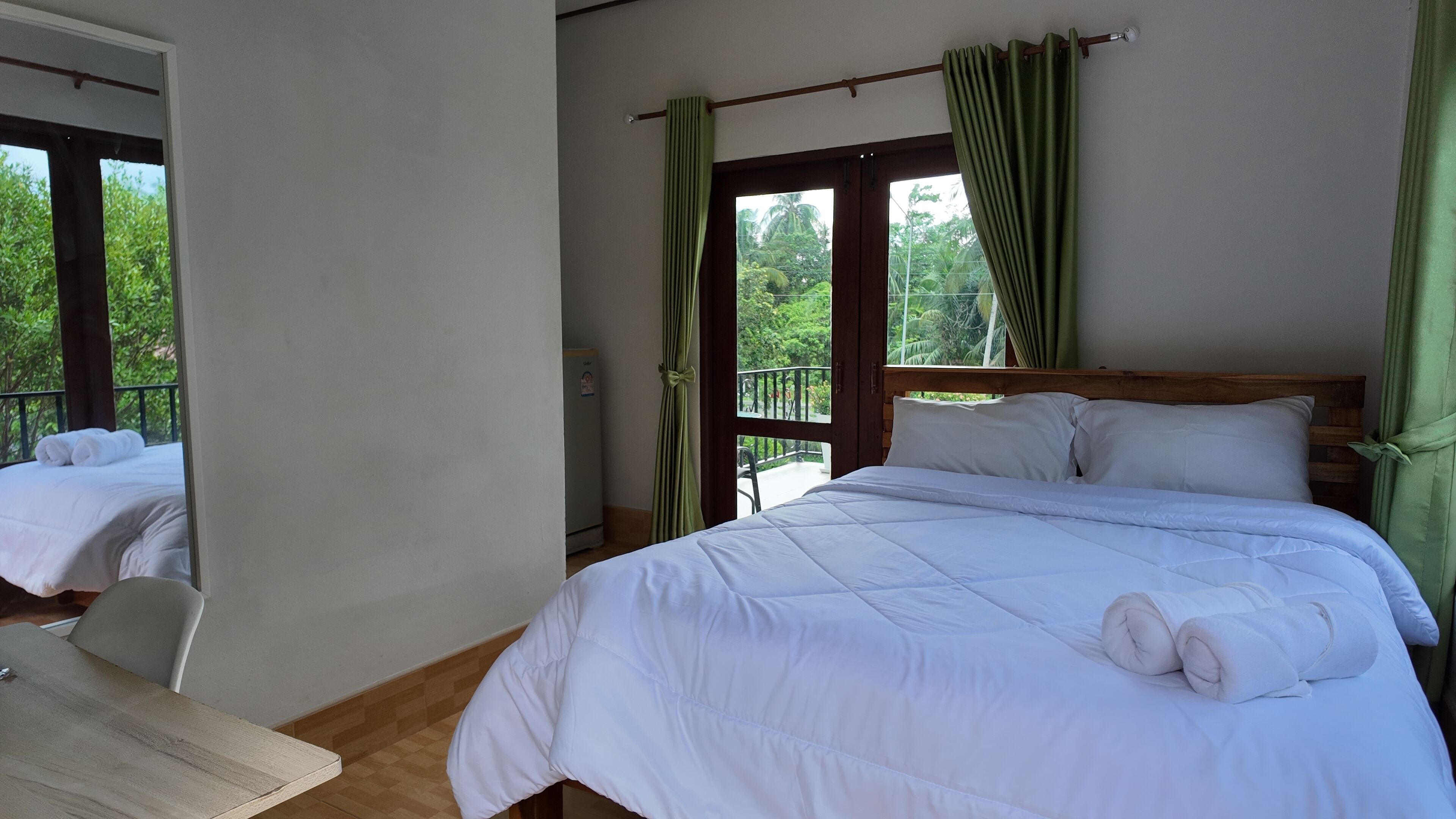 Quarto de hotel com cama, uma cadeira e vista para o verde pela janela.