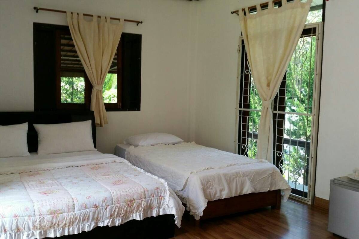 A room with two beds, a small table, and a window with curtains.