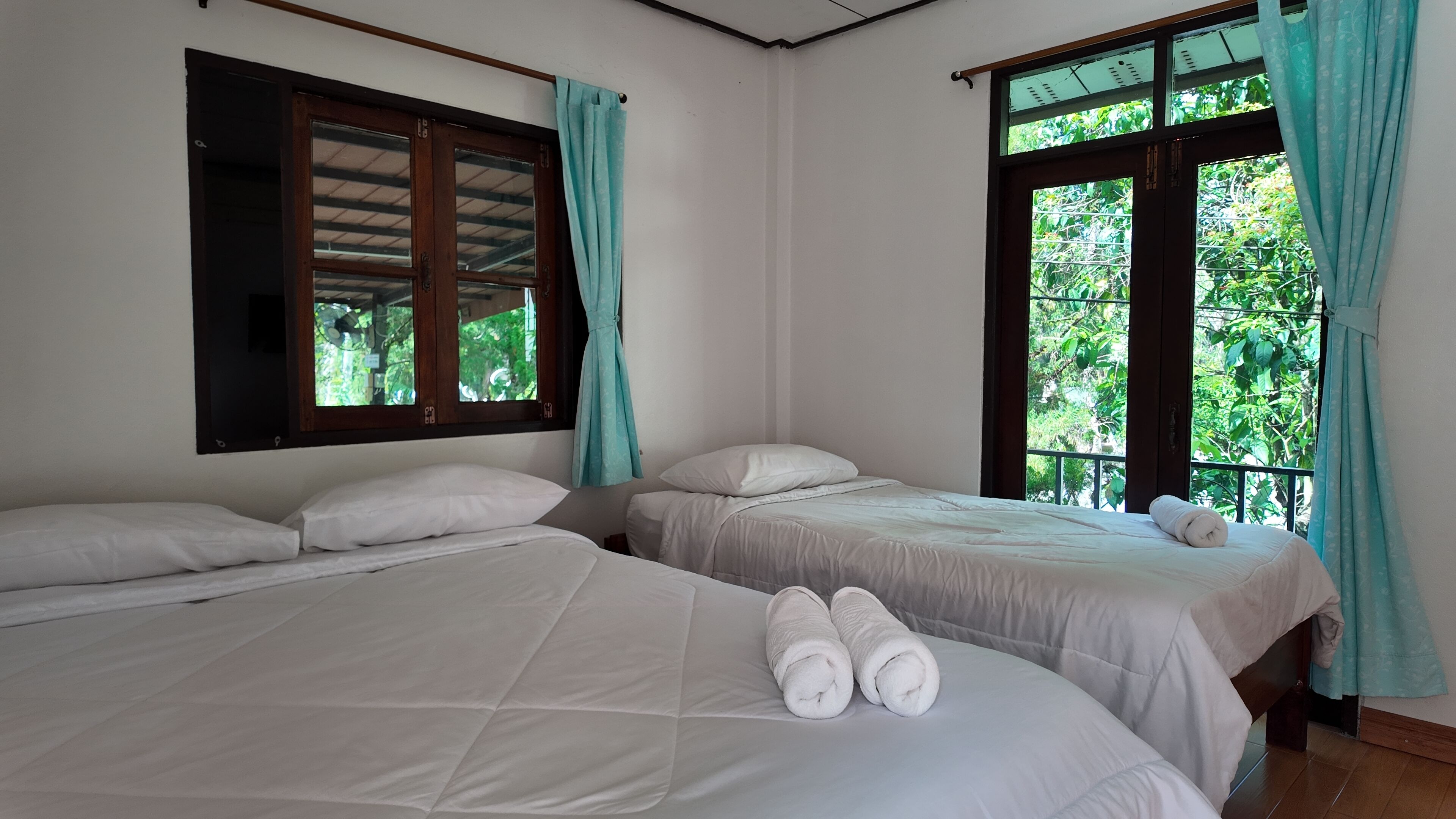 Een kamer met twee bedden, elk voorzien van witte lakens en kussens, een raam met gordijnen en uitzicht op groen buiten.