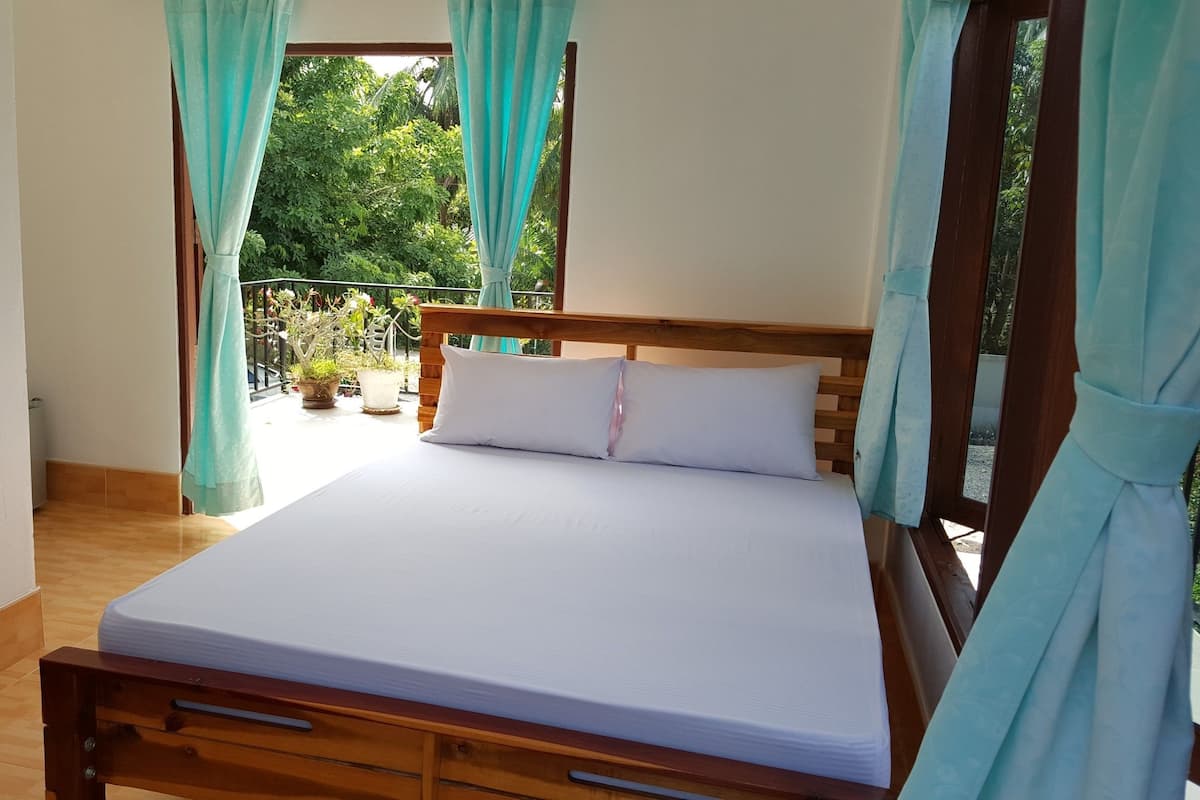 A bedroom with a wooden bed, white bedding, and a view of a balcony with potted plants.