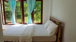Une chambre à coucher avec un lit, des rideaux et une vue sur la verdure par la fenêtre.