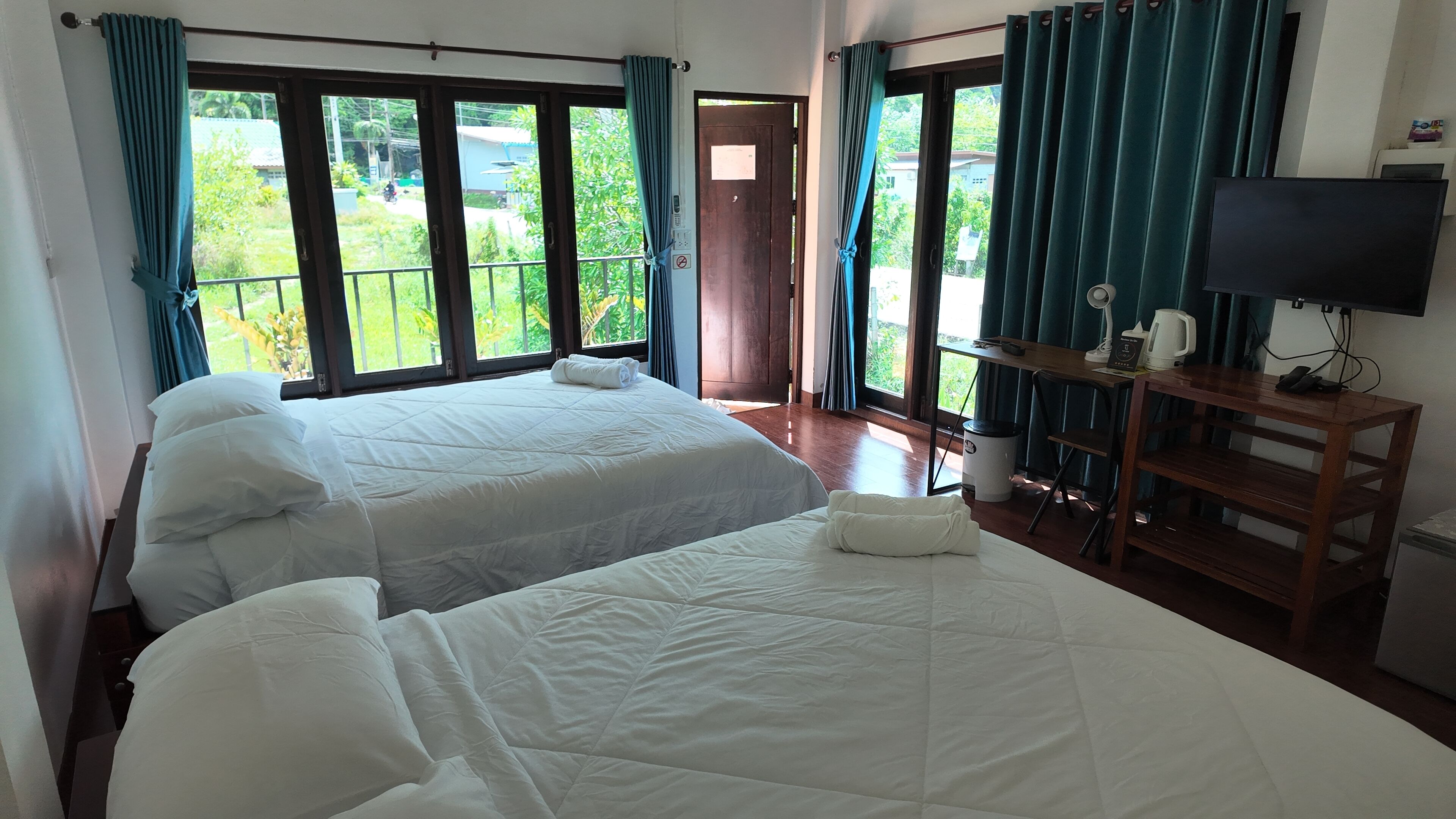 Una habitación de hotel con dos camas, televisor y balcón con cortinas.