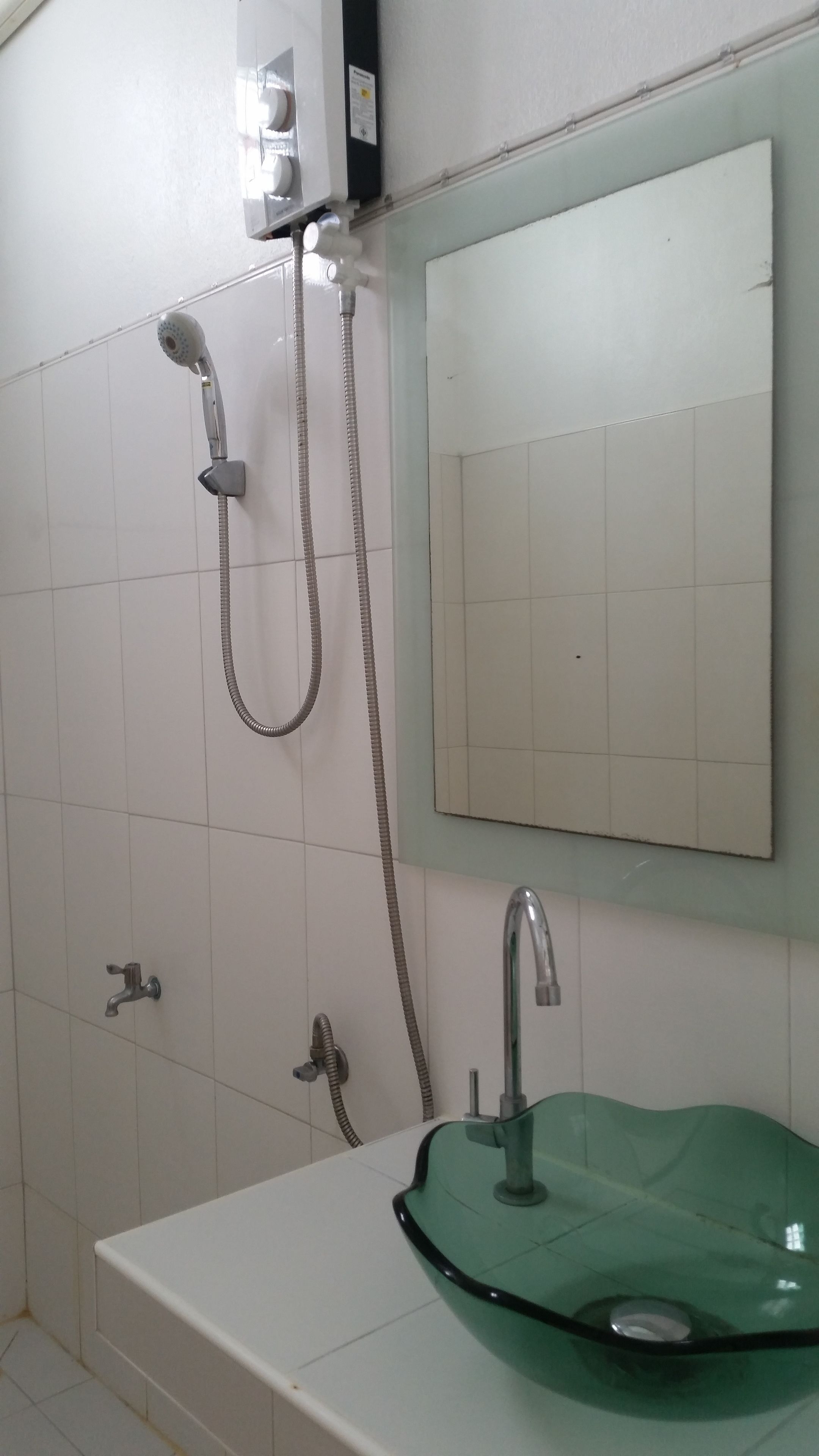 A bathroom with a white sink, a green glass basin, a mirror, and a shower with a handheld showerhead and a hose.
