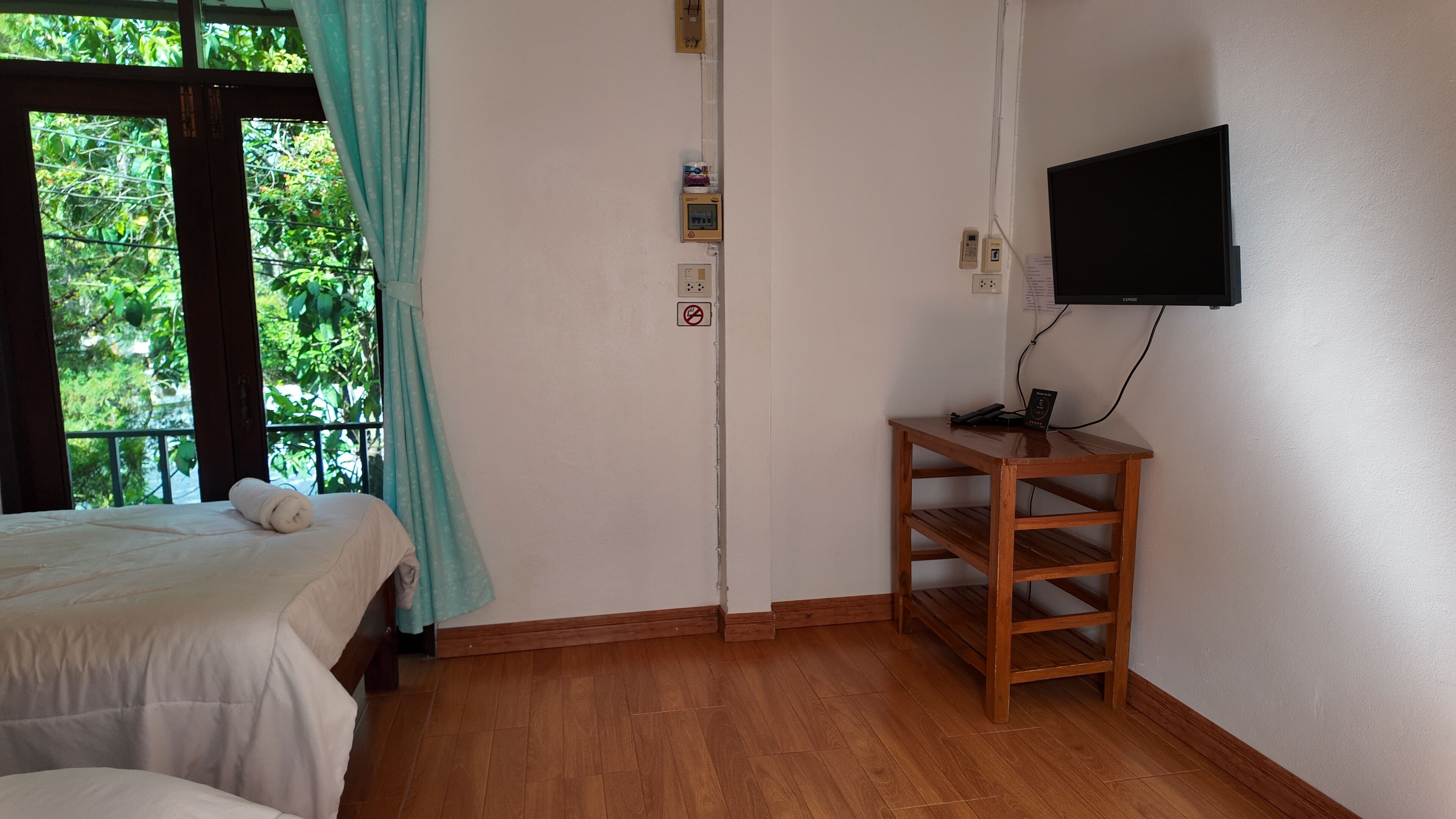 Una habitación con cama, una mesa de madera, televisor montado en la pared y una ventana con cortinas.